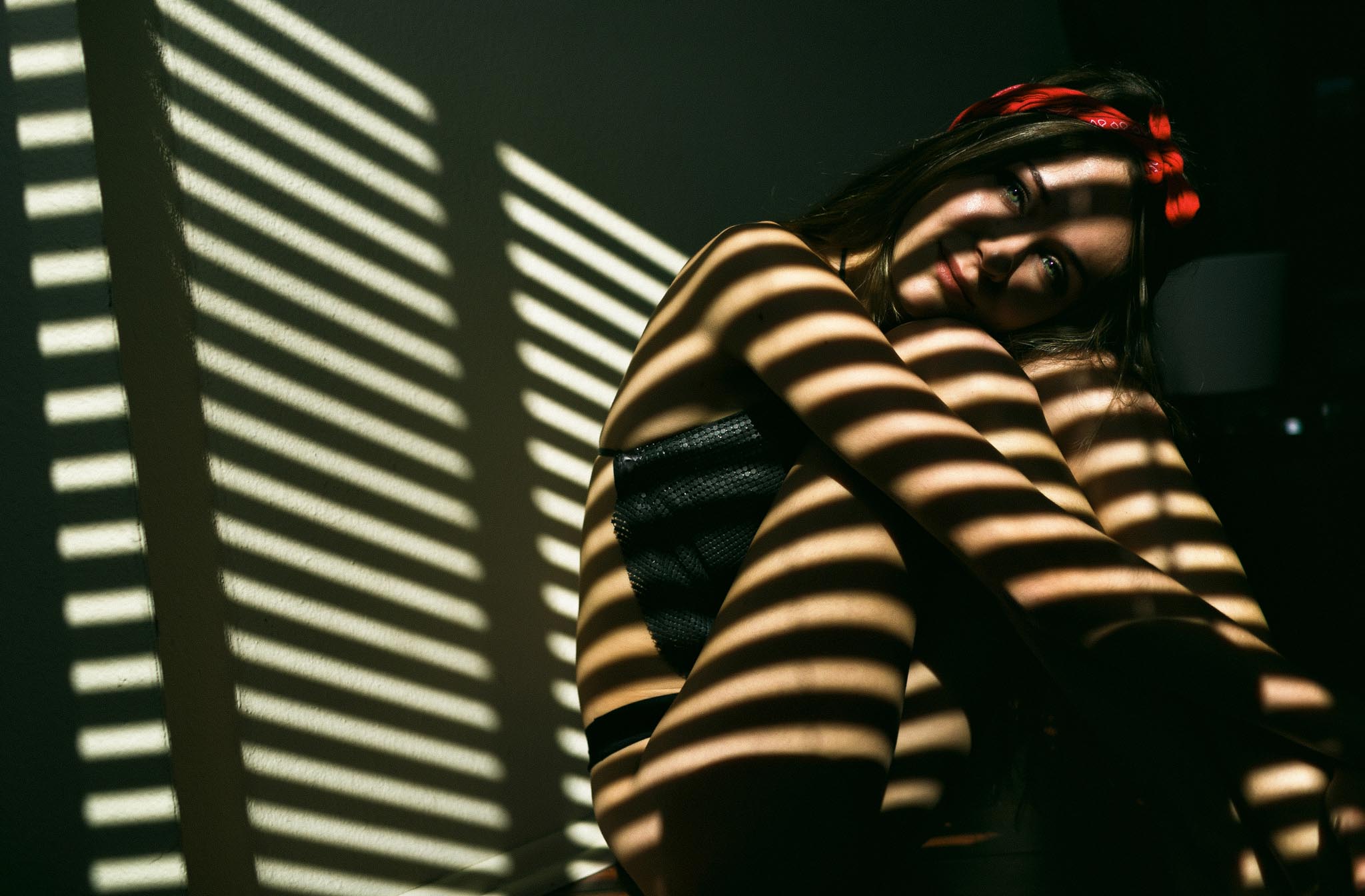 Artistic natural light boudoir photography featuring creative shadow lines from window blinds and a model wearing a red bandana.