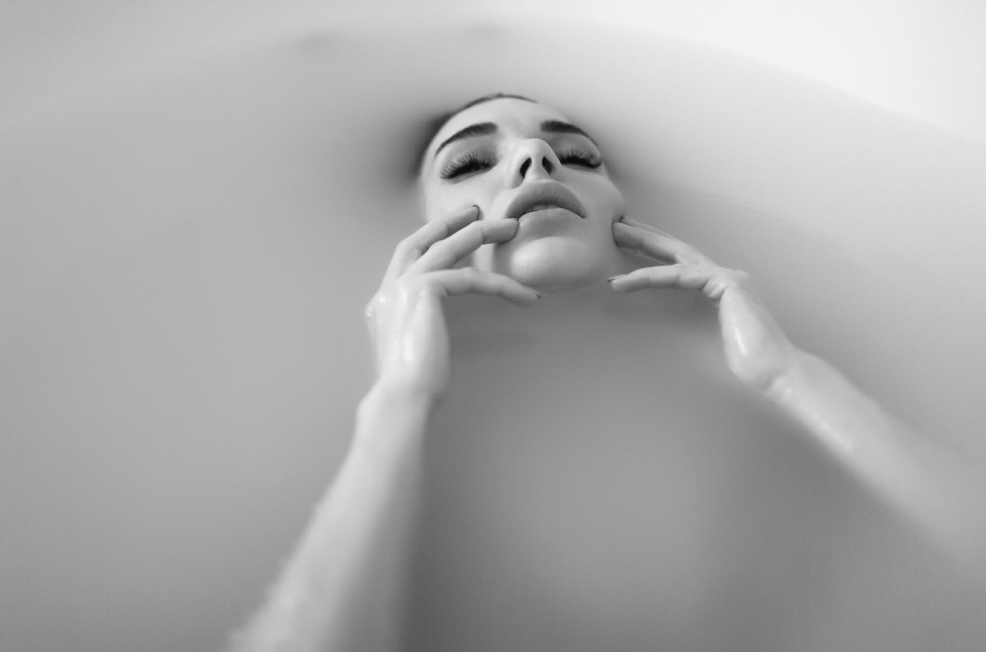 Fine art black and white milk bath boudoir portrait focusing on facial expression and hands